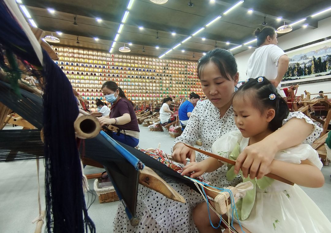 在“妈妈工坊”，从事织锦8年多的杨水莲在工余时间教5岁的女儿学习织锦。吴勇兵摄