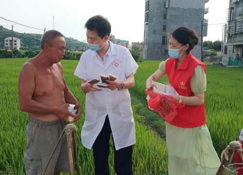 陈建军(中)深入田间地头宣传防暑知识,并为群众免费送去防暑药品。受访单位供图