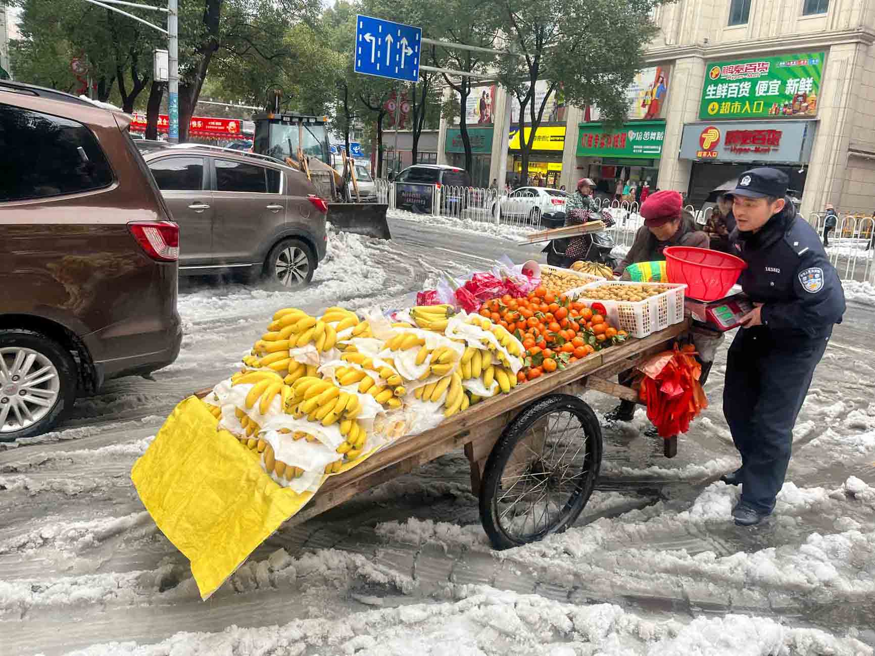 道路积雪难行，民警帮水果摊主推车。受访单位供图