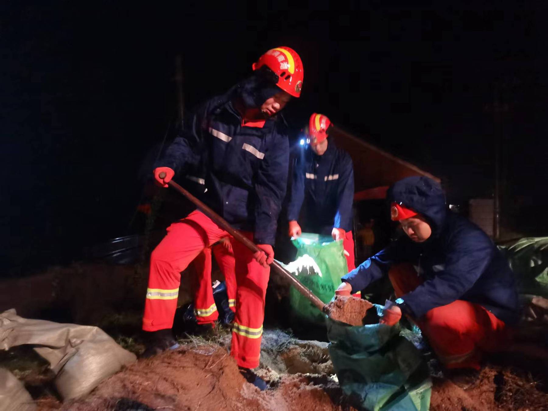 消防员在雨中装沙绑扎、传递沙袋加固防洪堤 (单位供图)