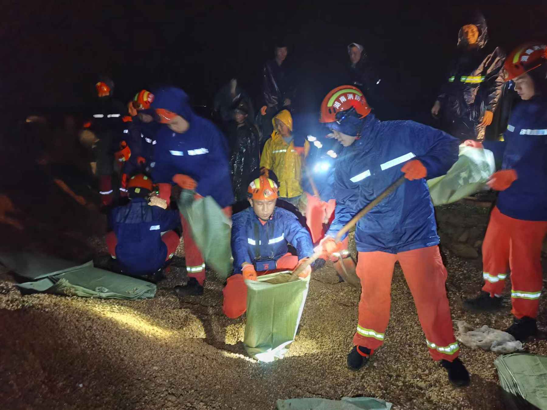 消防员在雨中装沙绑扎、传递沙袋加固防洪堤 (单位供图）