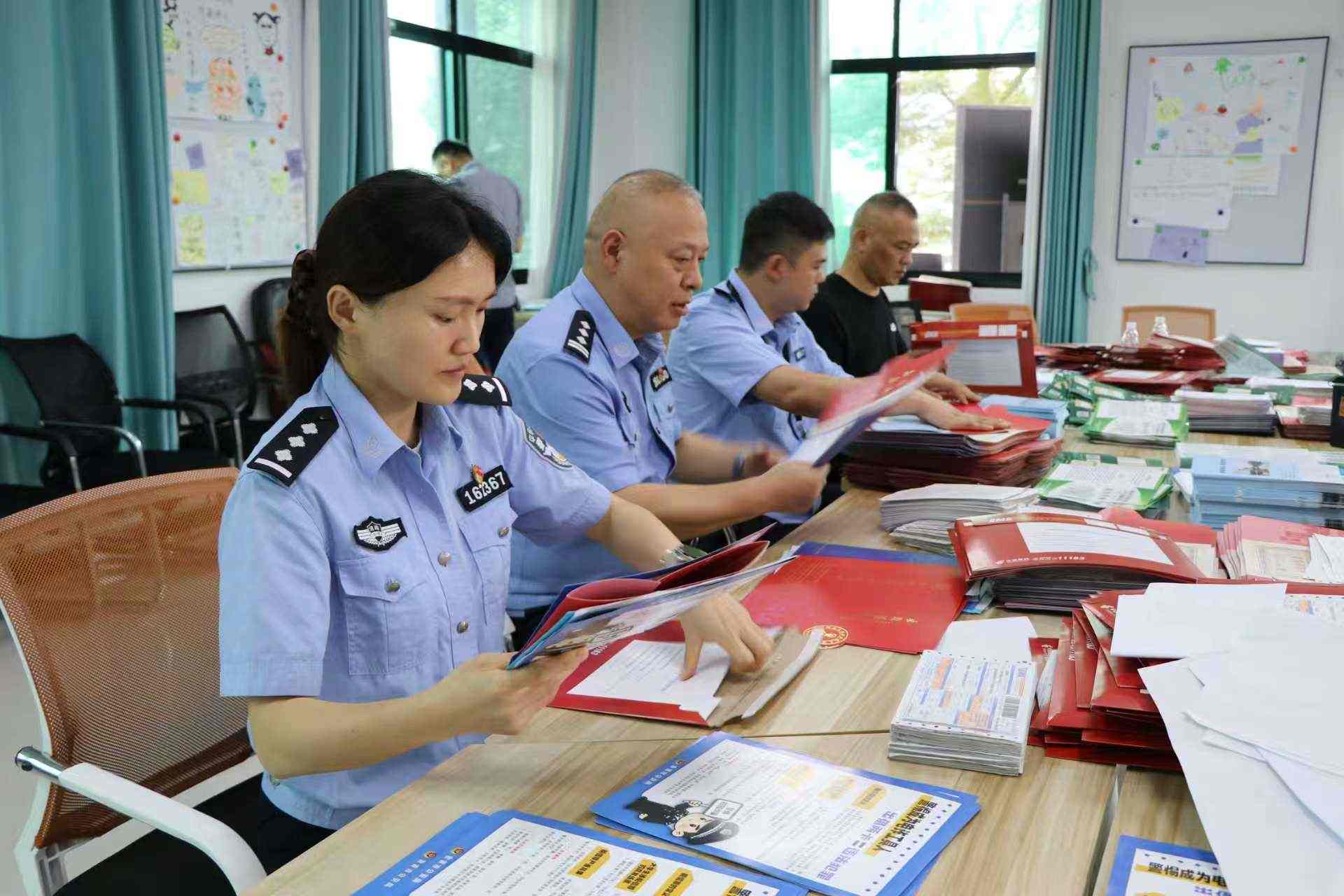 民警与学校工作人员一同将反诈宣传单装进录取通知书里（单位供图）