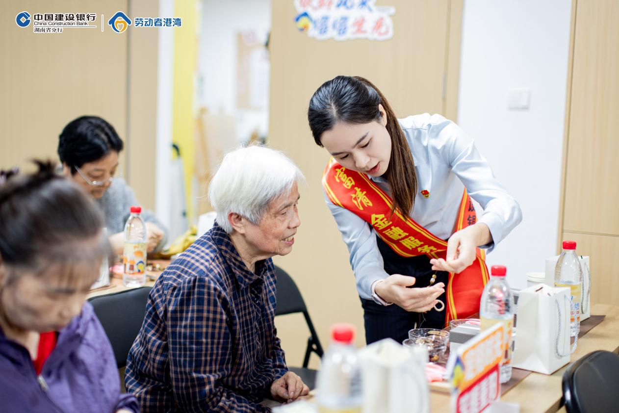 張富清金融服務隊志願者陪伴老人制作手工串珠。單位供圖